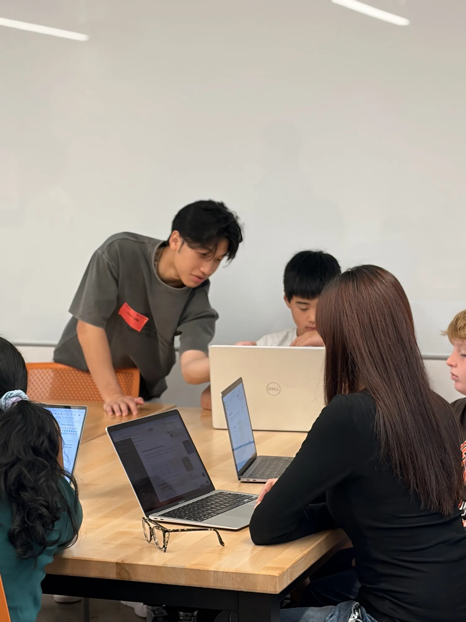 A university mentor leans over a table to help a student at his laptop