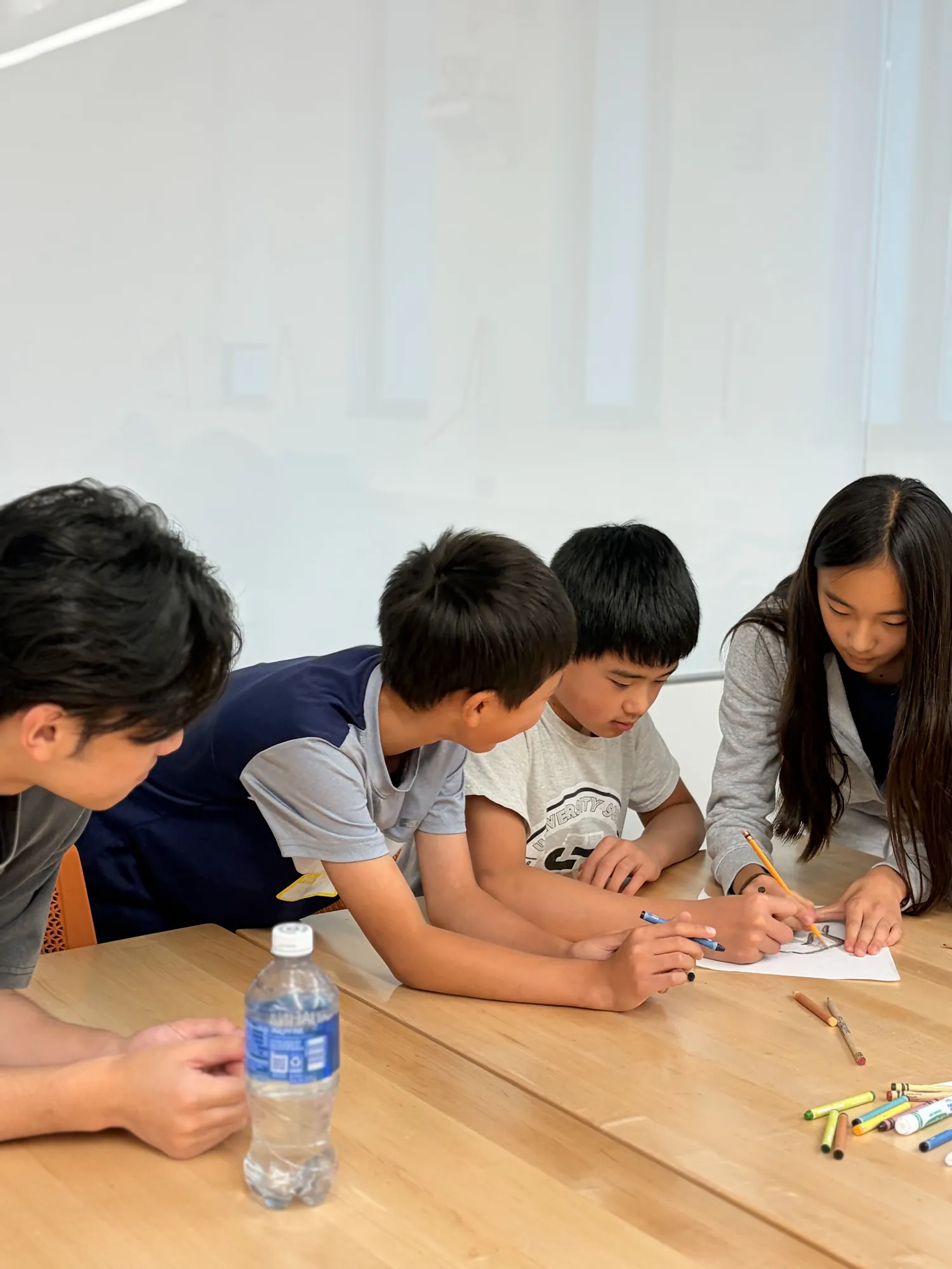 Four students lean over a table, sketching an idea together