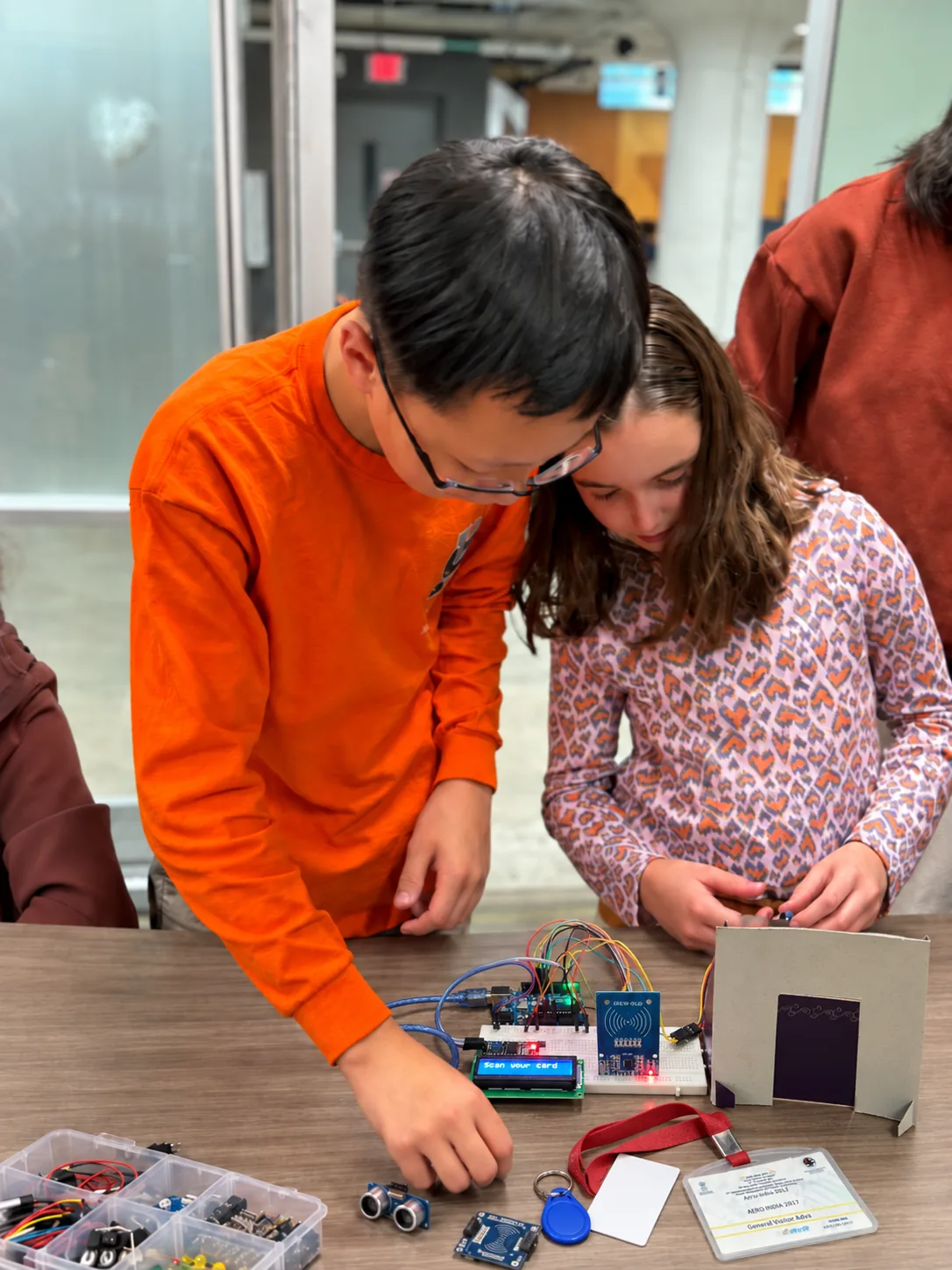 Two students wire an RFID card reader on a breadboard while its screen reads Scan your card